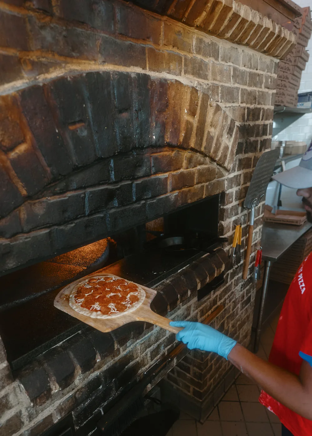 A pepperoni pie going into the brick oven on a wooden peel